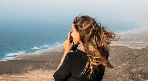 Frau steht in den Bergen am Meer und macht mit ihrer Kamera ein Foto von der Umgebung
