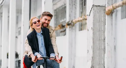 Mann und Frau fahren gemeinsam auf einem Fahrrad und lachen, daneben roter Kreis mit dem Text "Neu"