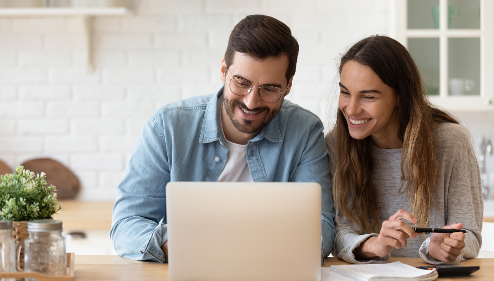 Frau und Mann sitzen in der Küche nebeneinander und schauen in einen Laptop