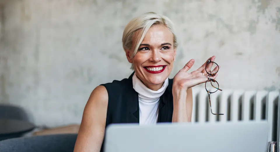 Blonde Frau sitzt vor ihrem Laptop und schaut in die Ferne