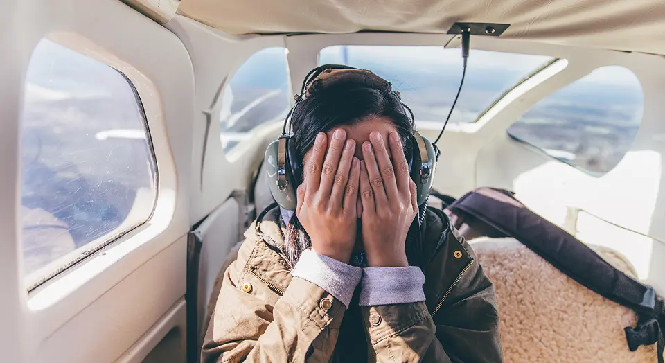 Frau sitzt in kleinem Flugzeug und hält sich die Augen zu