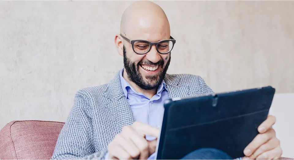 Mann in Businessklamotten sitzt vor seinem Tablet und lacht